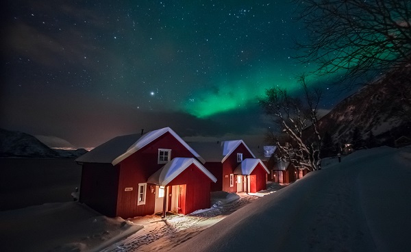 ISL-HELISKIING Northern lights over the red snowed-in cottages in Lapland village shutterstock 524142598